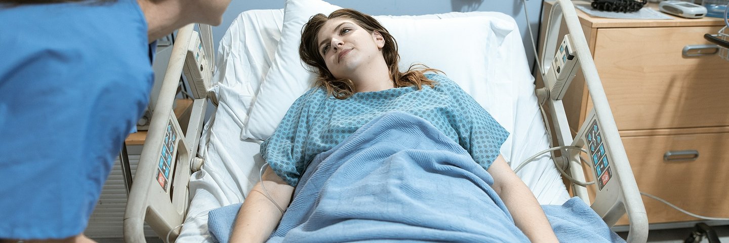 Situation im Kraneknehaus: Eine Pflegektaft beugt sich über ein im Bett liegende Patientin