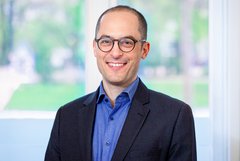 Das Bild zeigt einen freundlich lächelnden Mann mit einer Brille.