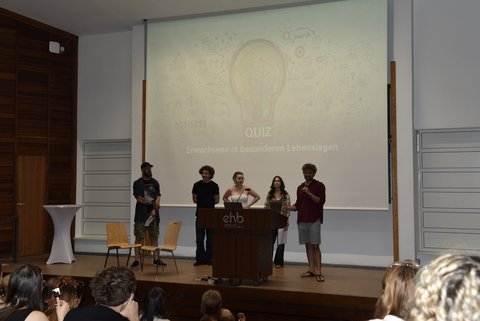 Verschiedene Personen stehen auf der Bühne und sprechen ins Publikum.