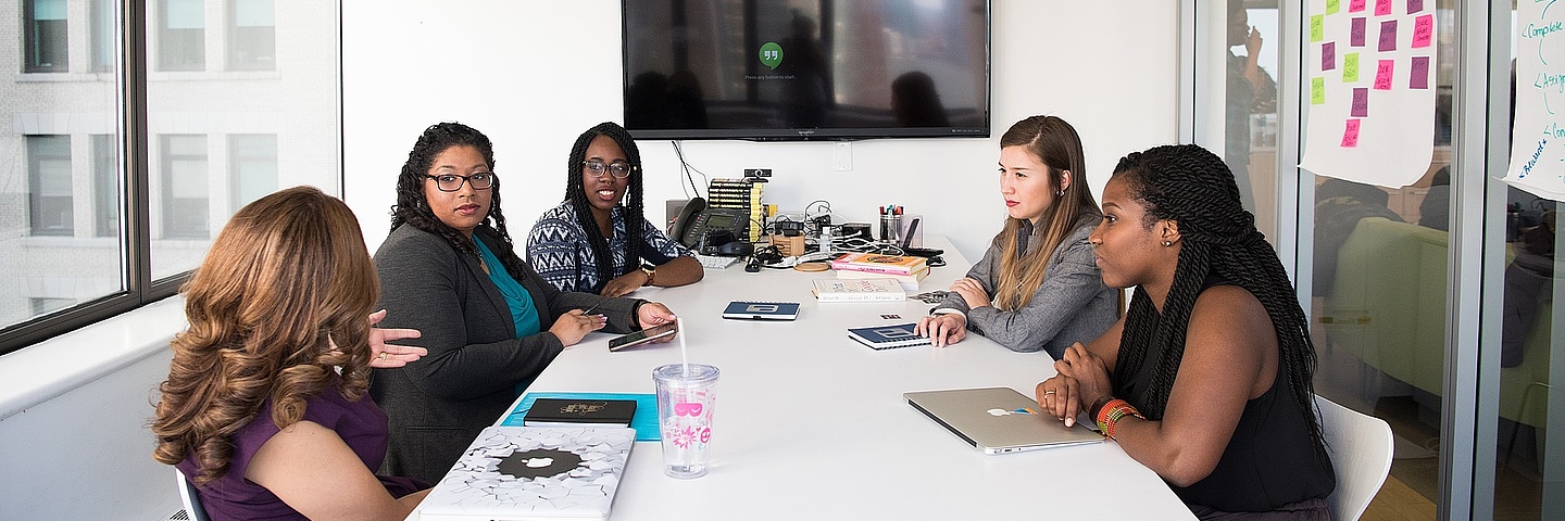 Fünf Frauen sitzen um einen Tisch im Besprechungszimmer und beraten