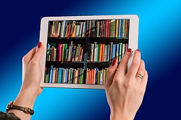 Zwei Hände halten ein Tablet, auf dem ein mit Büchern gefülltes Regal abgebildet ist