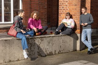 Vier junge Menschen unterhalten sich vor eine Backsteinhaus