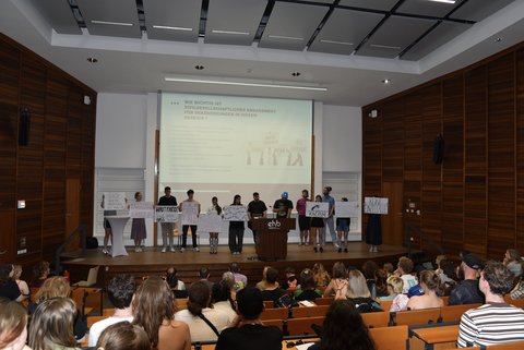 Verschiedene Personen stehen auf der Bühne und halten Plakate hoch.