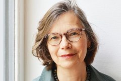Das Bild zeigt eine Frau, die eine Brille trägt und freundlich in die Kamera lächelt.