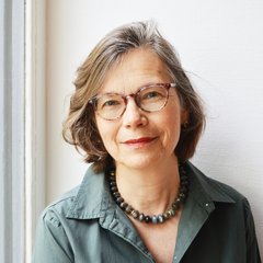 Das Bild zeigt eine Frau, die eine Brille trägt und freundlich in die Kamera lächelt.