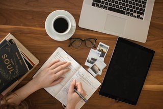 schreibtisch mit Laptop, Kaffeetasse, Brille, Bücher, Tablet