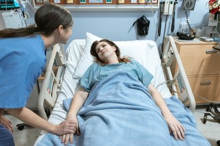 Situation im Kraneknehaus: Eine Pflegektaft beugt sich über ein im Bett liegende Patientin