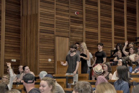 Zwei Personen stehen im Publikum und sprechen zur Bühne gewandt.