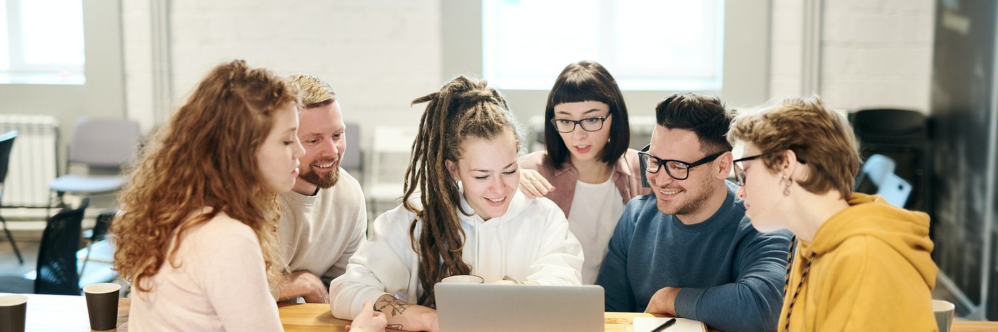 Ein Gruppe junger Leute sitzt zusammen um einen Laptop