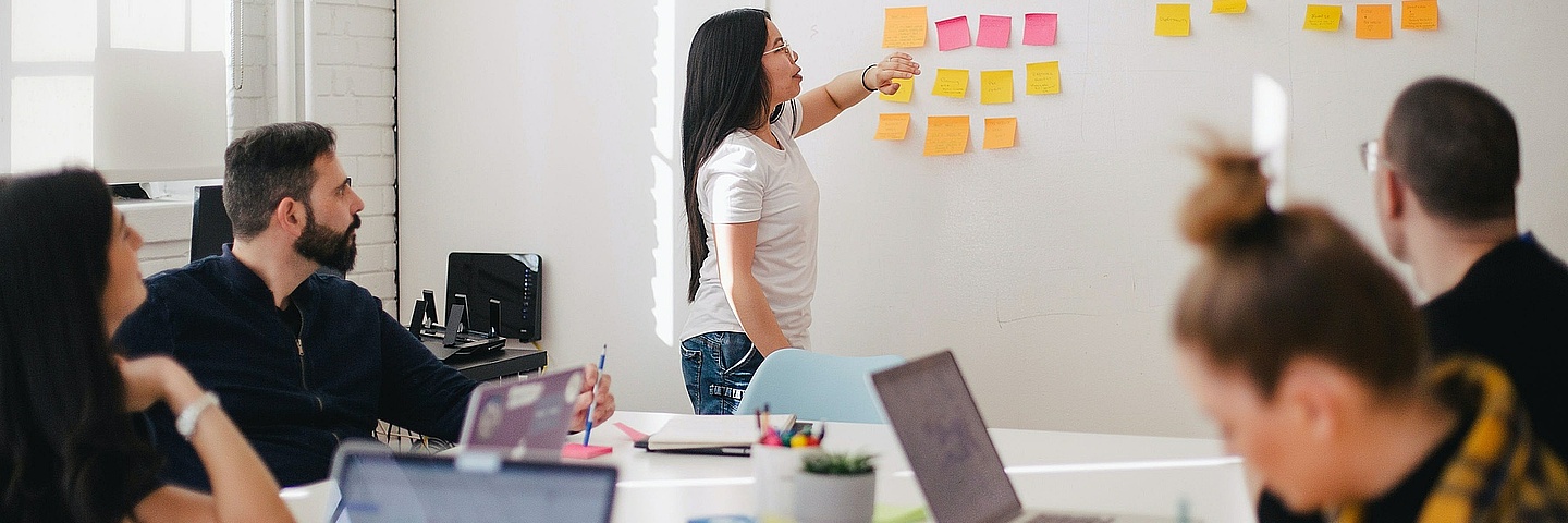 Headerbild - Seminarraum mit Studierenden die zusammen etwas erarbeiten mit Post-its an der Wand.