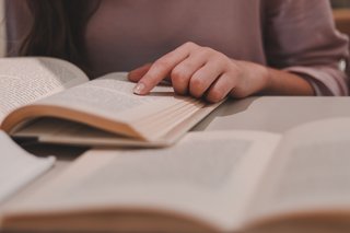 Das Bild zeigt ein aufgeschlagenes Buch in dem eine Person mit ihrem Finger auf etwas deutet.