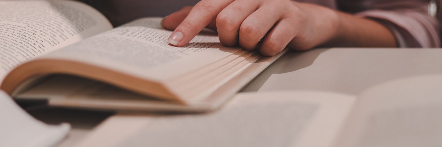 Das Bild zeigt ein aufgeschlagenes Buch in dem eine Person mit ihrem Finger auf etwas deutet.