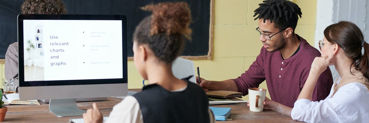 Junge Menschen sitzen in einem Klassenzimmer an Tischen vor dem Bildschirm