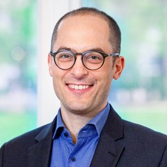 Das Bild zeigt einen freundlich lächelnden Mann mit einer Brille.