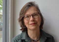 Das Bild zeigt eine Frau, die eine Brille trägt und freundlich in die Kamera lächelt.
