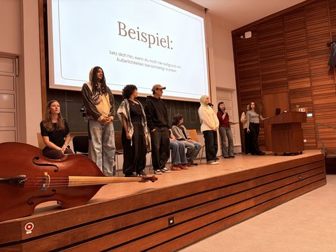 Das Bild zeigt einige Personen auf der Bühne des Audimax die etwas präsentieren.