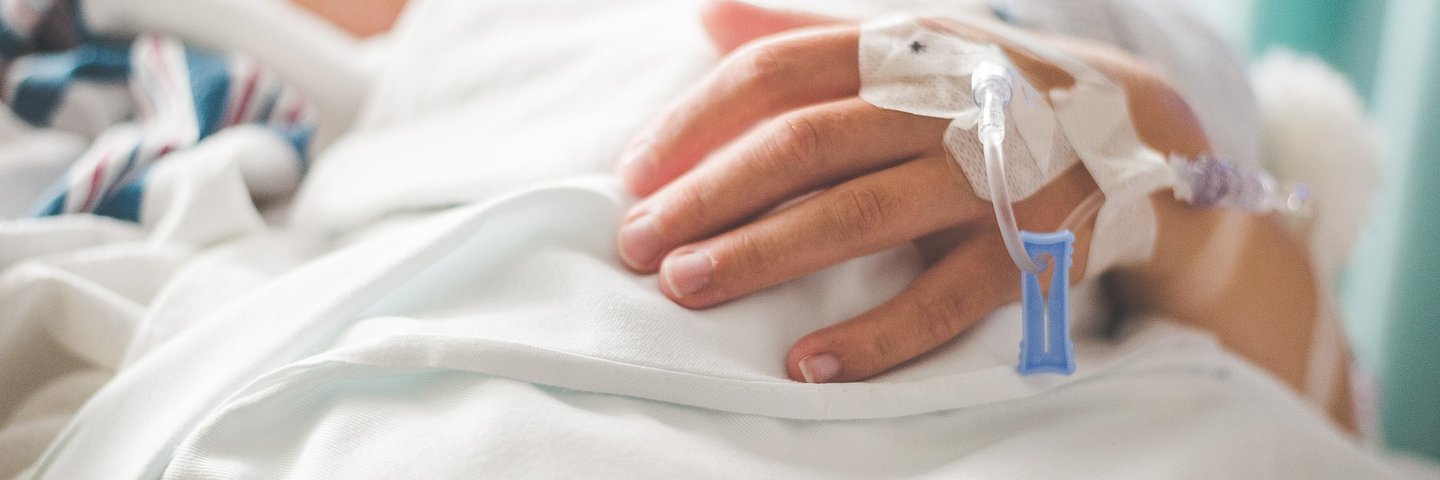 Eine Person im Krankenhausbett mit Infusion in der Hand