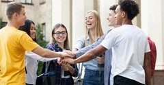 Studierende stapeln ihre Hände als Zeichen von Teamgeist auf dem Campus. iStock