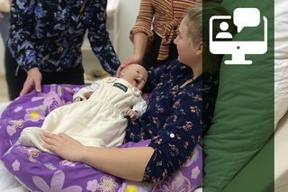 Das Bild zeigt eine Frau mit einem Stillkissen und einer Babypuppe