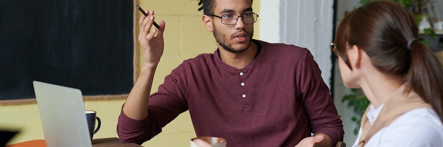 Ein Mann und eine Frau sitzen einander zugewandt an einem Tisch vor sich einen Laptop