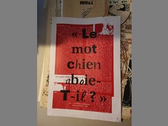 Eine Rote Tafel mit schwarzen großen Shriftzügen. Darunter weiße sehr kleine Schrift. Beides lässt sich nur schwer entziffern